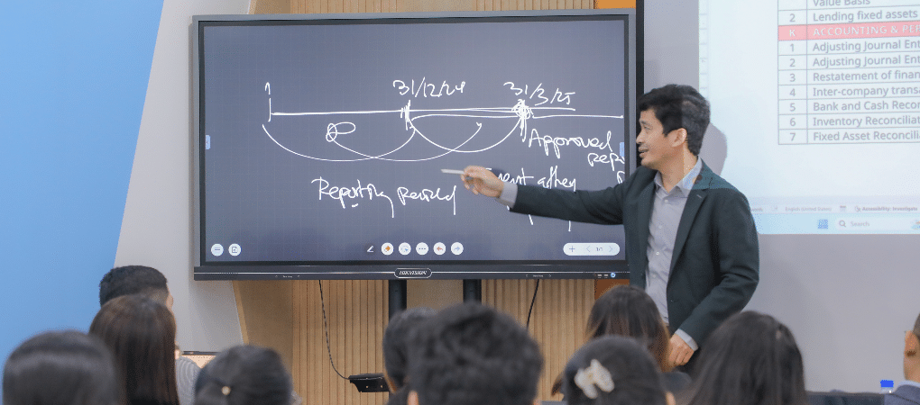 Mr. Sim Chankiriroth, Vice President of YEAC, pointing to a diagram on an interactive whiteboard that explains the financial reporting period and approval process during a training session for Cambodian entrepreneurs.