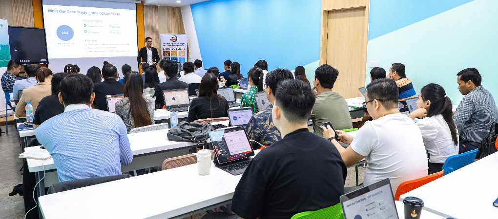 A speaker presents a case study on "SME Solutions Ltd." to Cambodian entrepreneurs during a business strategy workshop.